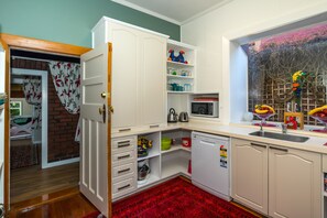 A compact kitchen with white cabinets, a microwave, and a sink. There is a red patterned rug on the floor. - The Sanctuary Beach Side (Timaru)