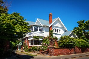 A two-story house with a prominent brick chimney, white siding, and a bay window. - The Sanctuary Beach Side (Timaru)