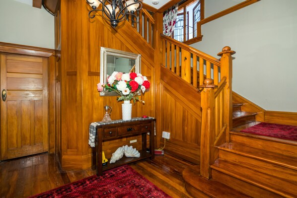 A wooden staircase with a red carpet, a console table with a vase of flowers, and a mirror above it. - The Sanctuary Beach Side (Timaru)