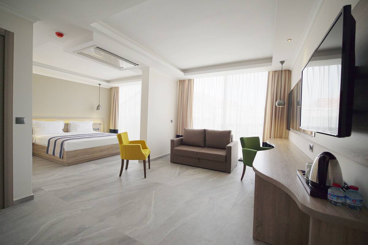 Una habitación de hotel con una cama, un sofá, un escritorio con espejo y un televisor.