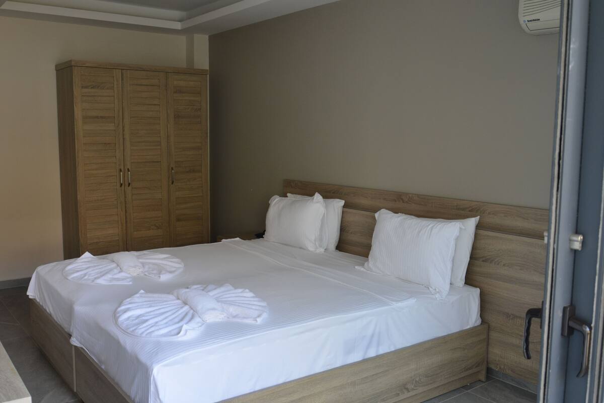 Una cama bien hecha con ropa blanca y toallas, un cabecero de madera y un armario a la izquierda.