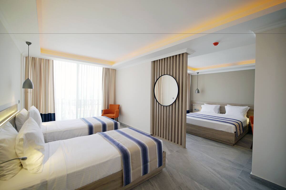 Habitación de hotel con dos camas, un espejo redondo, una silla y una mesita de noche.