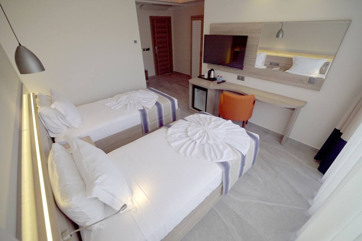 Habitación de hotel con dos camas individuales, un escritorio con televisor y un pequeño rincón de descanso.