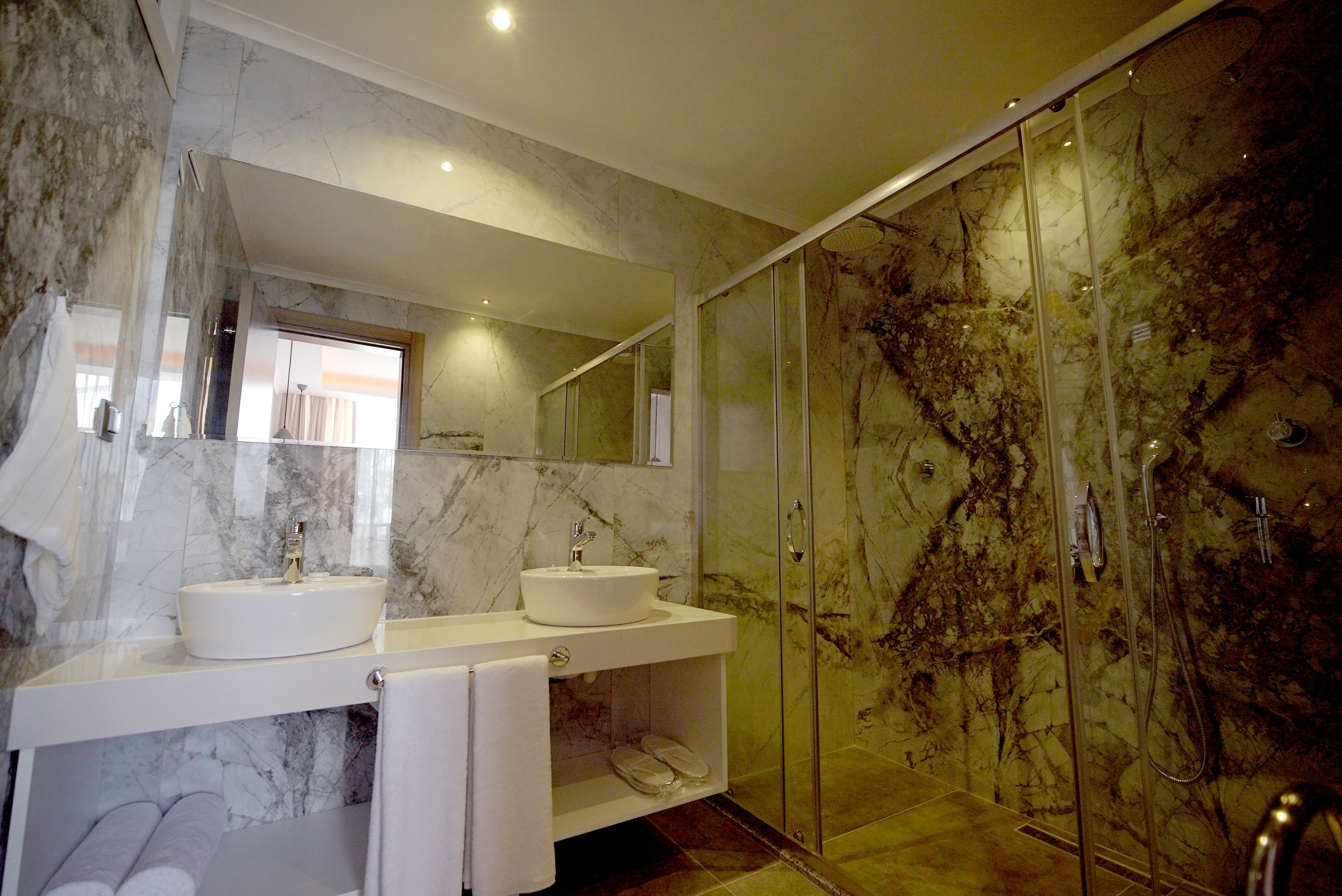 Een moderne badkamer met twee wastafels, een douchecabine van glas en marmeren wanden.