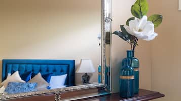A bedroom with a blue headboard, a mirror, a vase with a white flower, and two blue bottles on a wooden dresser.