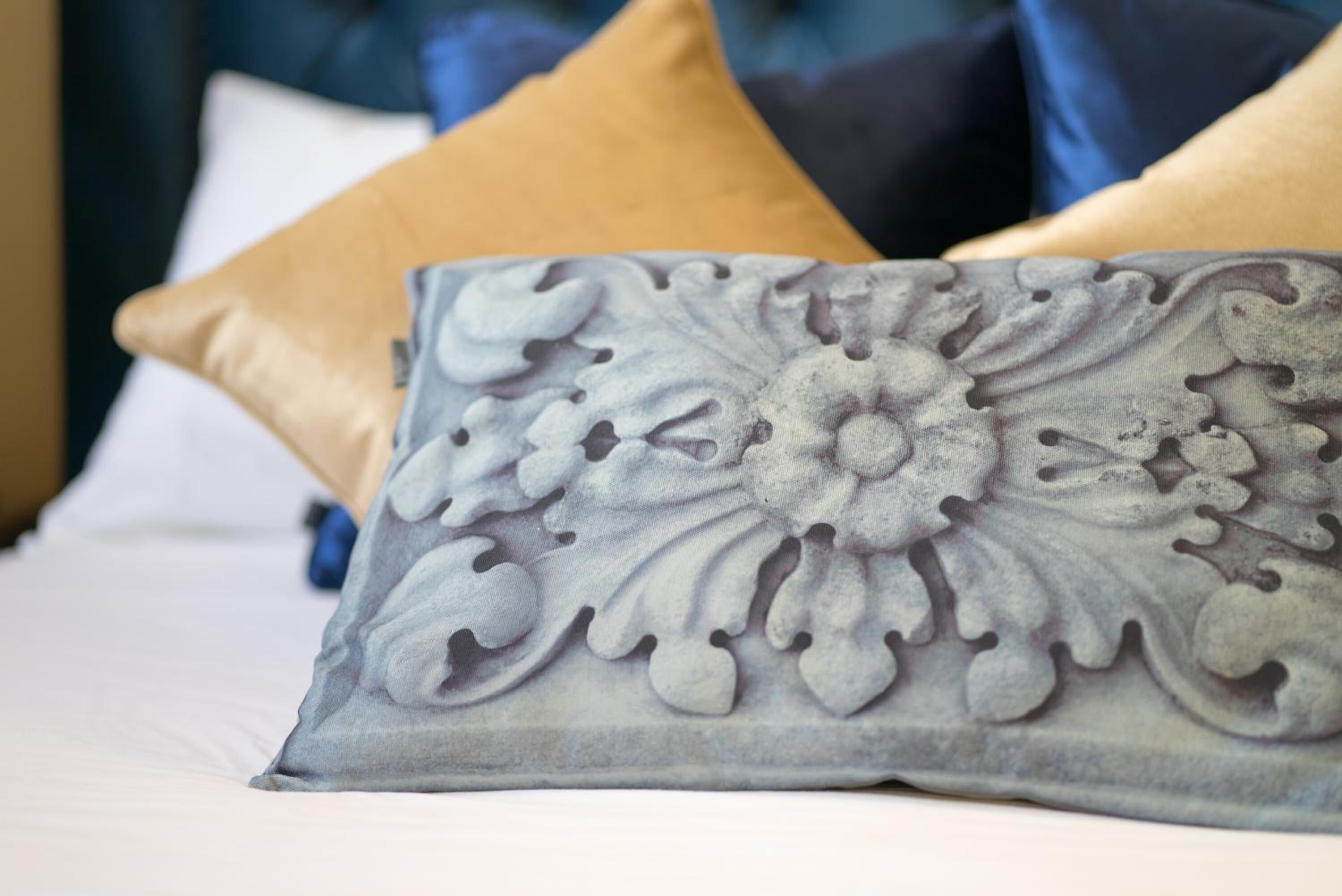 A bed with a decorative pillow featuring an embossed floral design.