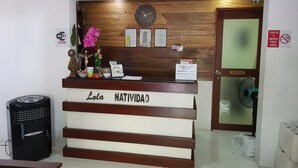 Un mostrador de recepción de hotel con fondo de madera, un reloj y varios carteles informativos.