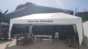 Un área de estar al aire libre con toldo, que incluye una mesa y sillas, identificada con el rótulo "Hotel Iola Navidad".