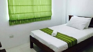 Una cama bien hecha con sábanas blancas y una colcha verde a rayas, un cabecero de madera y una persiana verde.