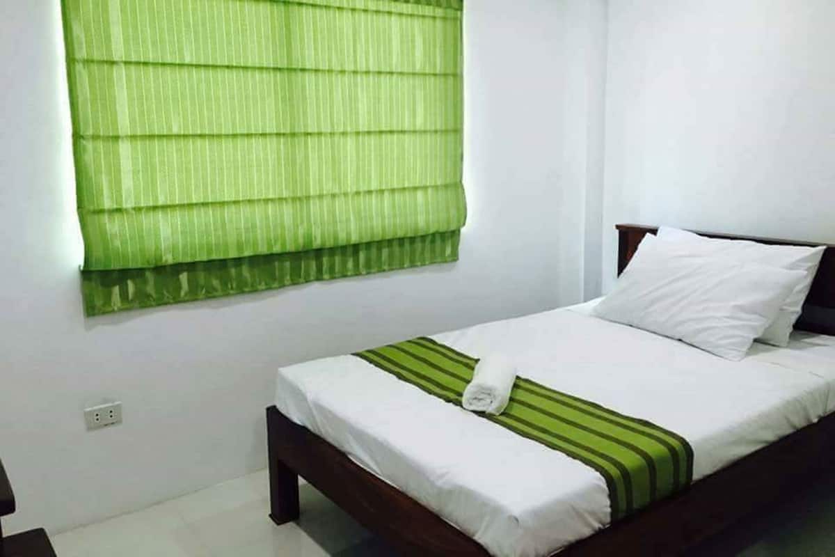 Una cama bien hecha con sábanas blancas y una colcha verde a rayas, un cabecero de madera y una persiana verde.