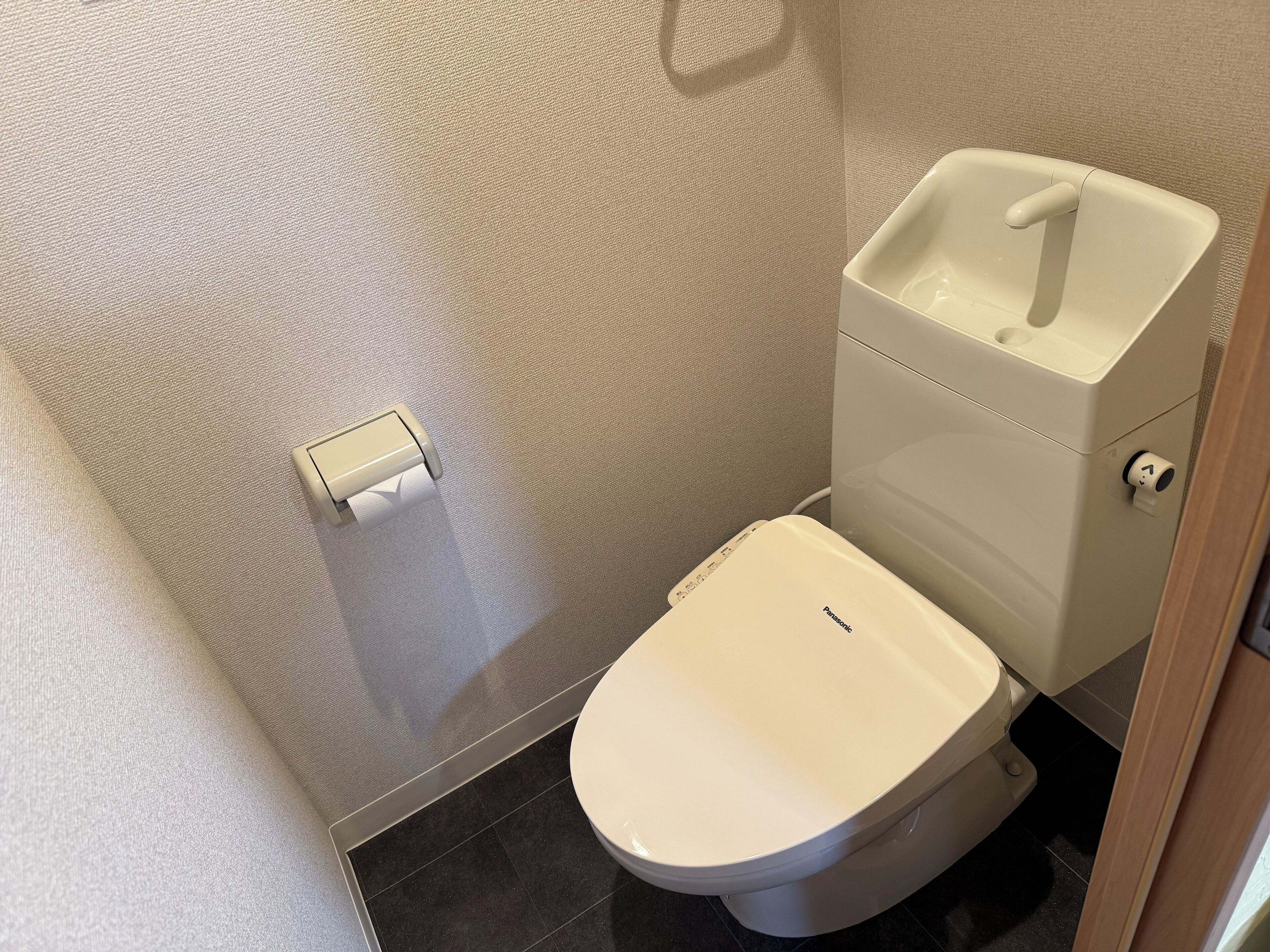 Uma casa de banho moderna com sanita, lavatório e dispensador de papel.