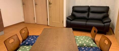 A room with a wooden table, four chairs with floral cushions, a black leather sofa, and wooden doors.
