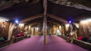 Ein Zimmer mit Holzboden und -wänden, das eine zentrale Säule, Bänke mit Kissen und einen violetten Teppich zeigt.