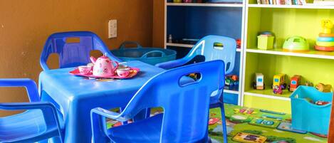 A children's play area with a table and chairs, a bookshelf, and a play mat with educational games.