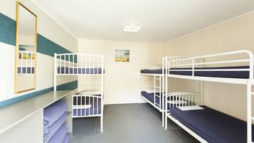 A room with bunk beds, a mirror, and a small shelf with pillows.