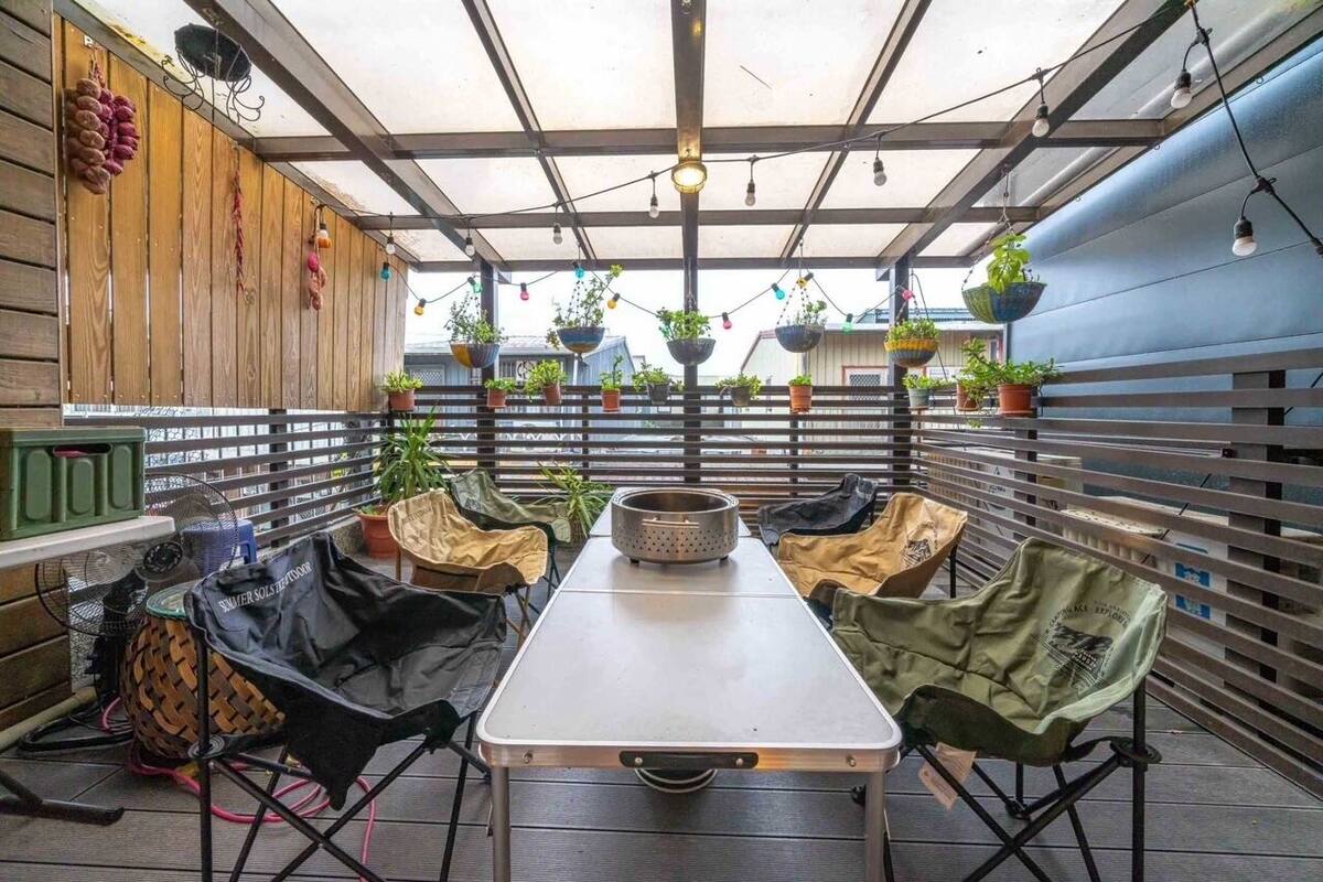 Ein überdachter Außenbereich mit Tisch, Stühlen, hängenden Pflanzen und einem Ventilator.
