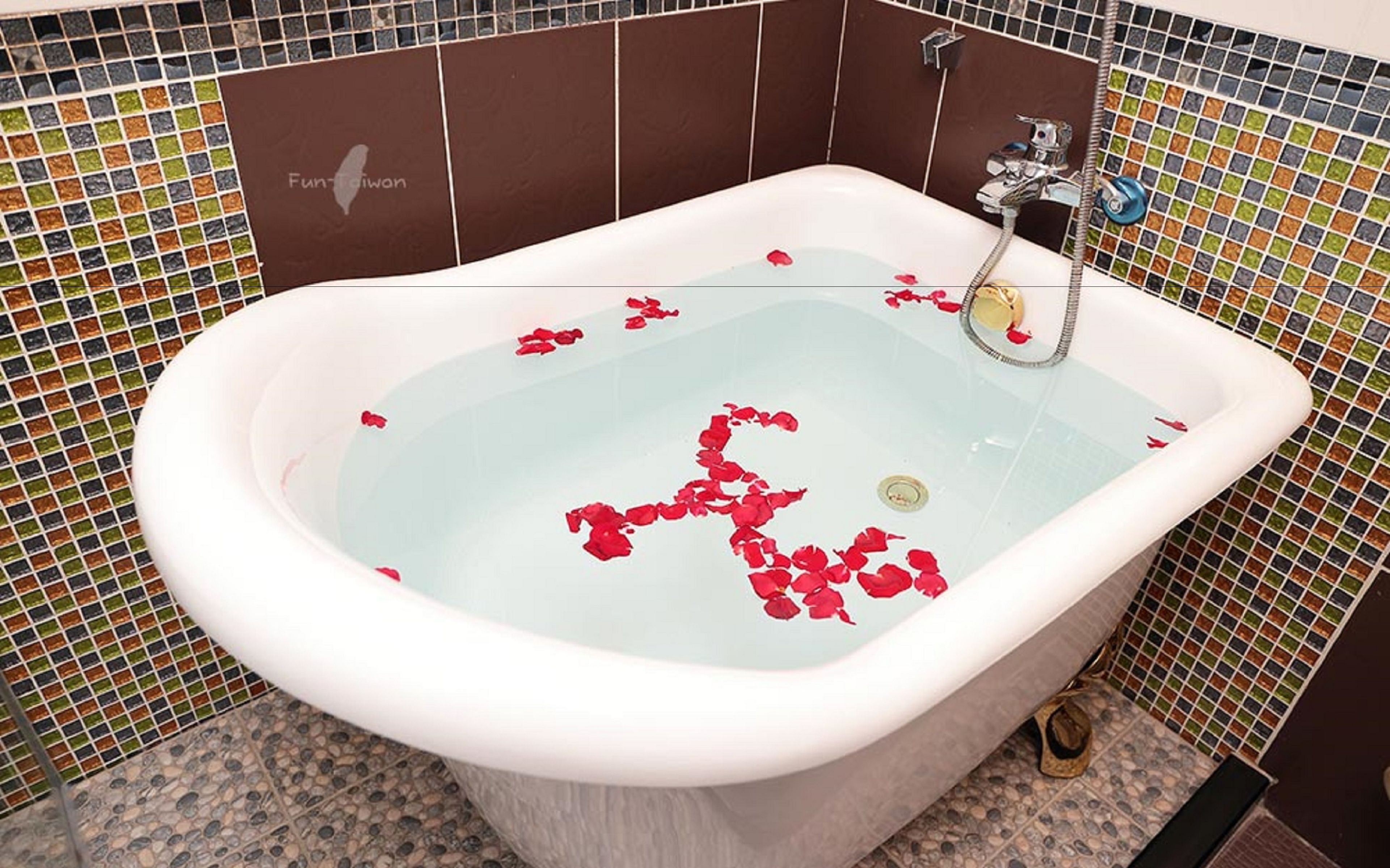 A bathtub with rose petals floating in the water, surrounded by mosaic tile walls.