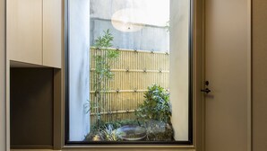 Uitzicht door een raam op een kamer met een bamboebordering, een kleine tuin en een traditionele Japanse lantaarn.