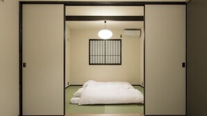 Een traditionele Japanse kamer met tatami vloerbedekking, een futon bed, een shoji scherm en een plafondlamp.
