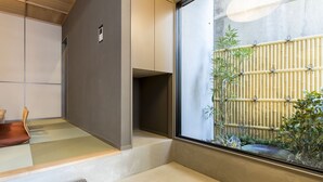 Een traditionele Japanse kamer met tatami vloerbedekking, een lage houten tafel en uitzicht op een bamboebos via een schuifdeur.