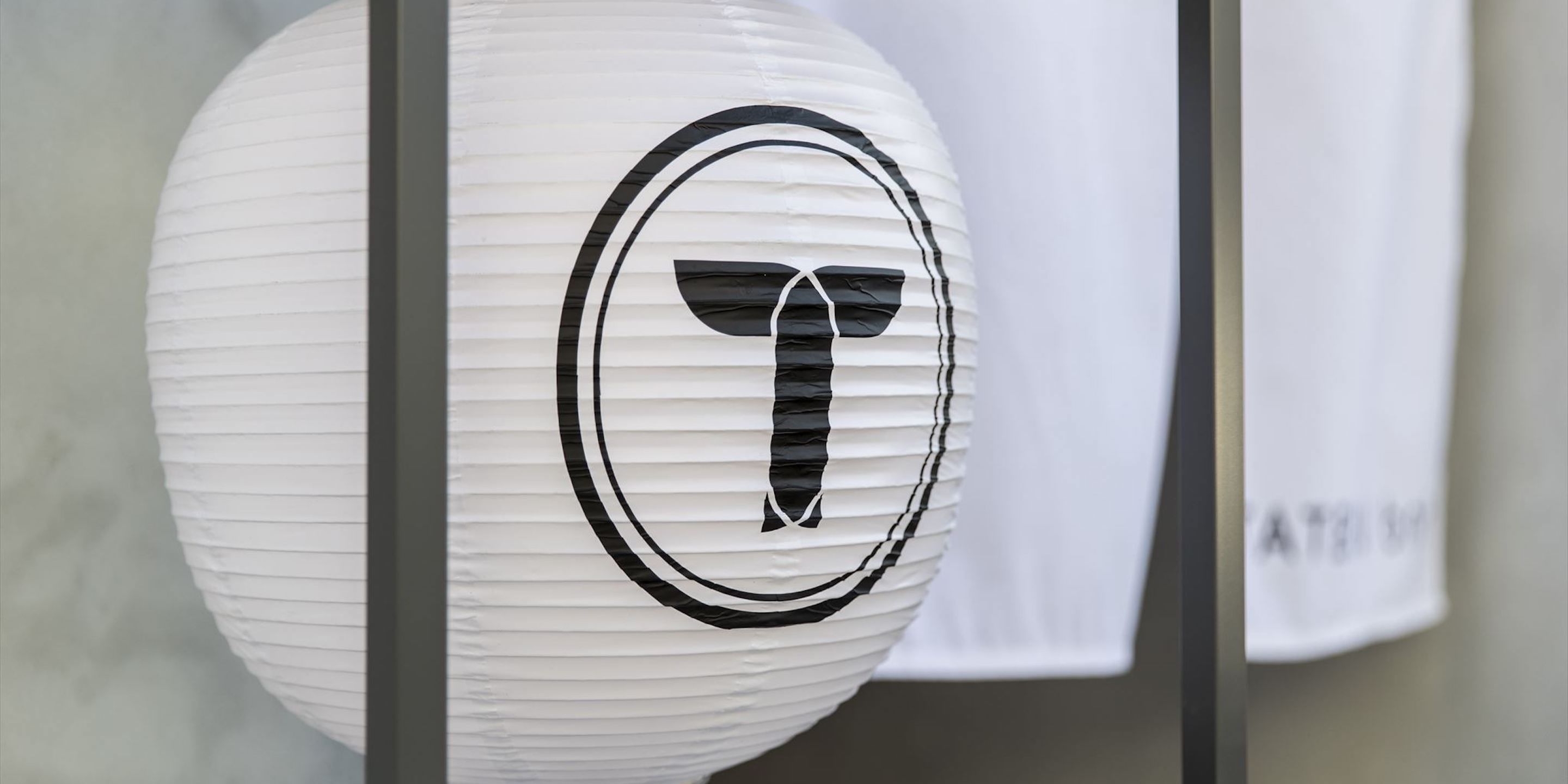 A white paper lantern with a black T-shaped logo.
