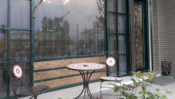 A patio with two metal tables and chairs, a large window with decorative ironwork, and a view of the street outside. - Starburst B&B (Dongshan)