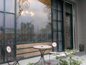 A patio with two metal tables and chairs, a large window with decorative ironwork, and a view of the street outside. - Starburst B&B (Dongshan)