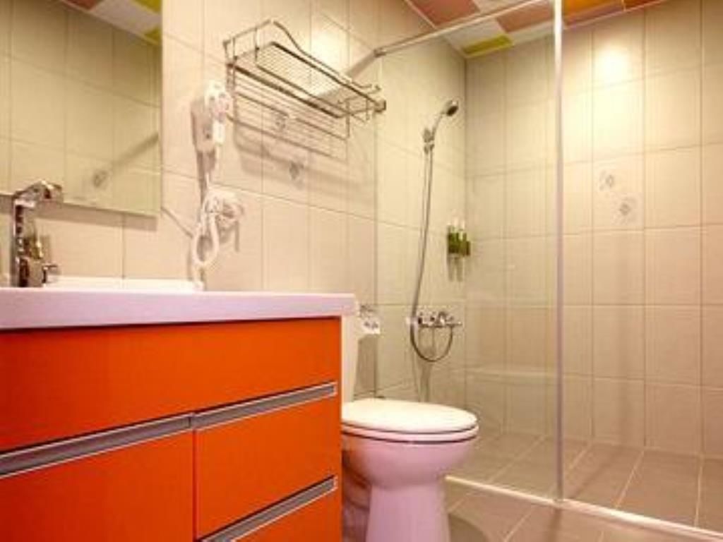 Une salle de bain avec des toilettes blanches, un meuble-lavabo orange et une cabine de douche en verre.