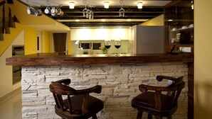A kitchen with a stone countertop, two wooden bar stools, hanging wine glasses, and a modern light fixture. - Starburst B&B (Dongshan)