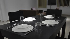 A dining table set with plates, cutlery, and glasses, with a television mounted on the wall in the background. - Best View Apartments (Nadi)