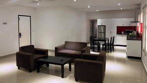 A modern living room with a sofa set, a coffee table, and a dining area with a table and chairs. There is a kitchen area with cabinets and a refrigerator. - Best View Apartments (Nadi)