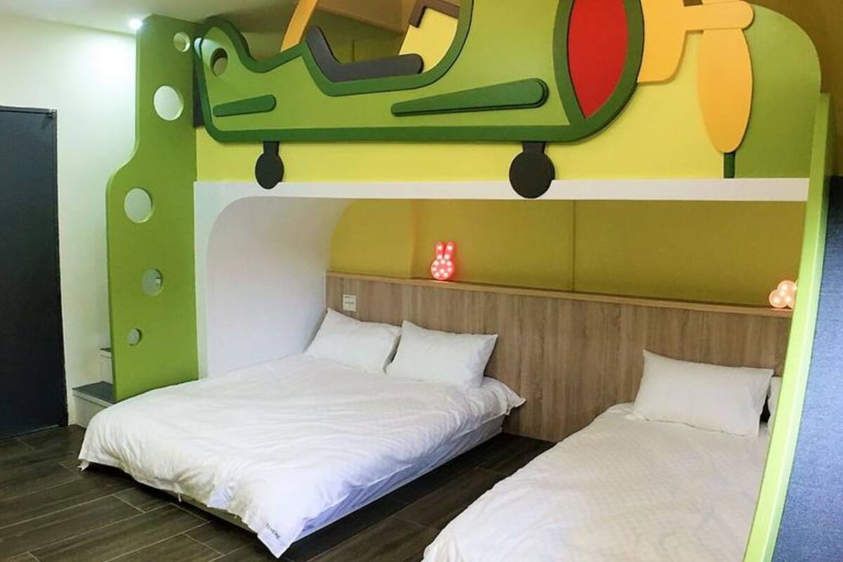 A room with two beds, a green airplane decoration on the wall, and a small red flower on the nightstand.