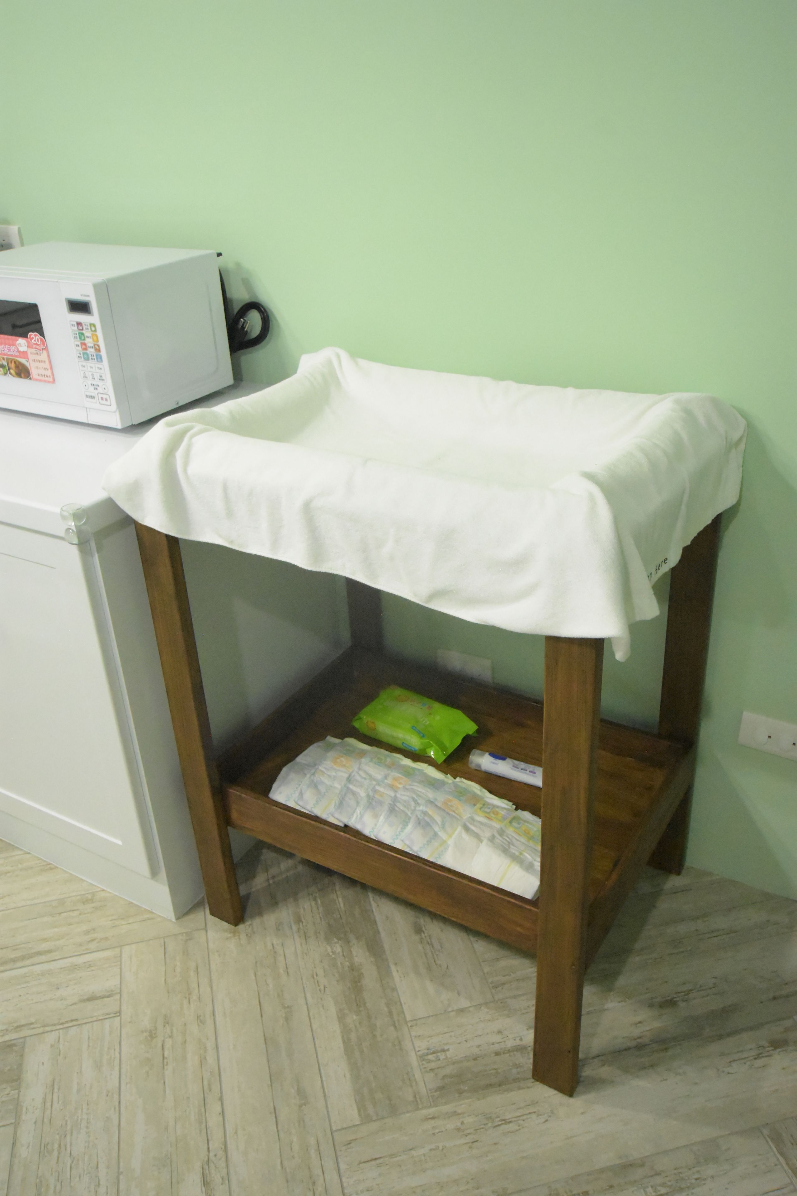Een houten tafeltje met een witte tafelkleed, een groene tas en een krant eronder.