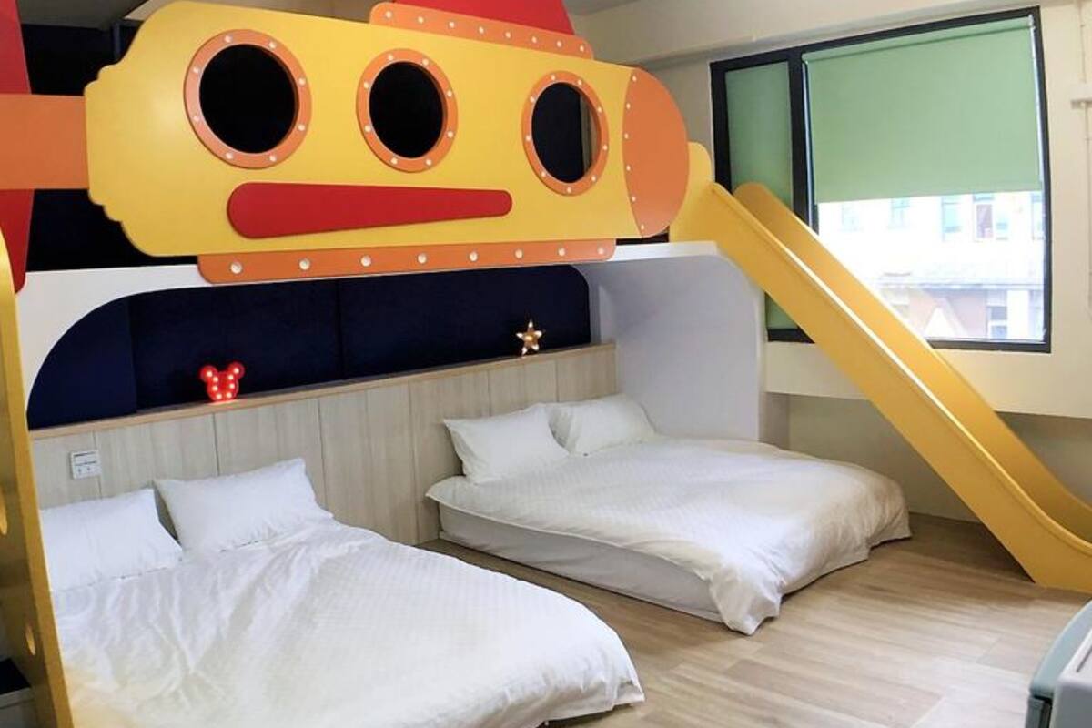 A children's room with bunk beds, a slide, and a window with a view of buildings.