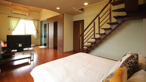Un dormitorio con una cama, televisión, una escalera y una puerta que da a otra habitación.