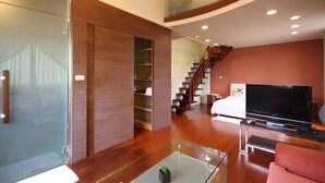Una sala de estar moderna con una mesa de centro de vidrio, un televisor de pantalla plana, un sofá y una escalera que conduce a un nivel superior.
