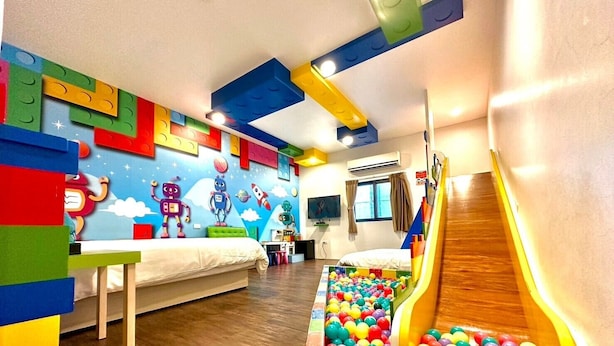 A children's playroom with a slide, colorful ball pit, and a bed with a white mattress.