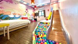 A children's playroom with a ball pit, a slide, and a bed with a colorful mural on the wall.