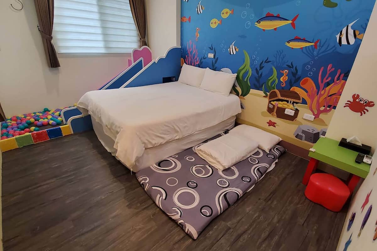 A child-friendly room with a bed, a play area with colorful balls, and an ocean-themed wall mural.