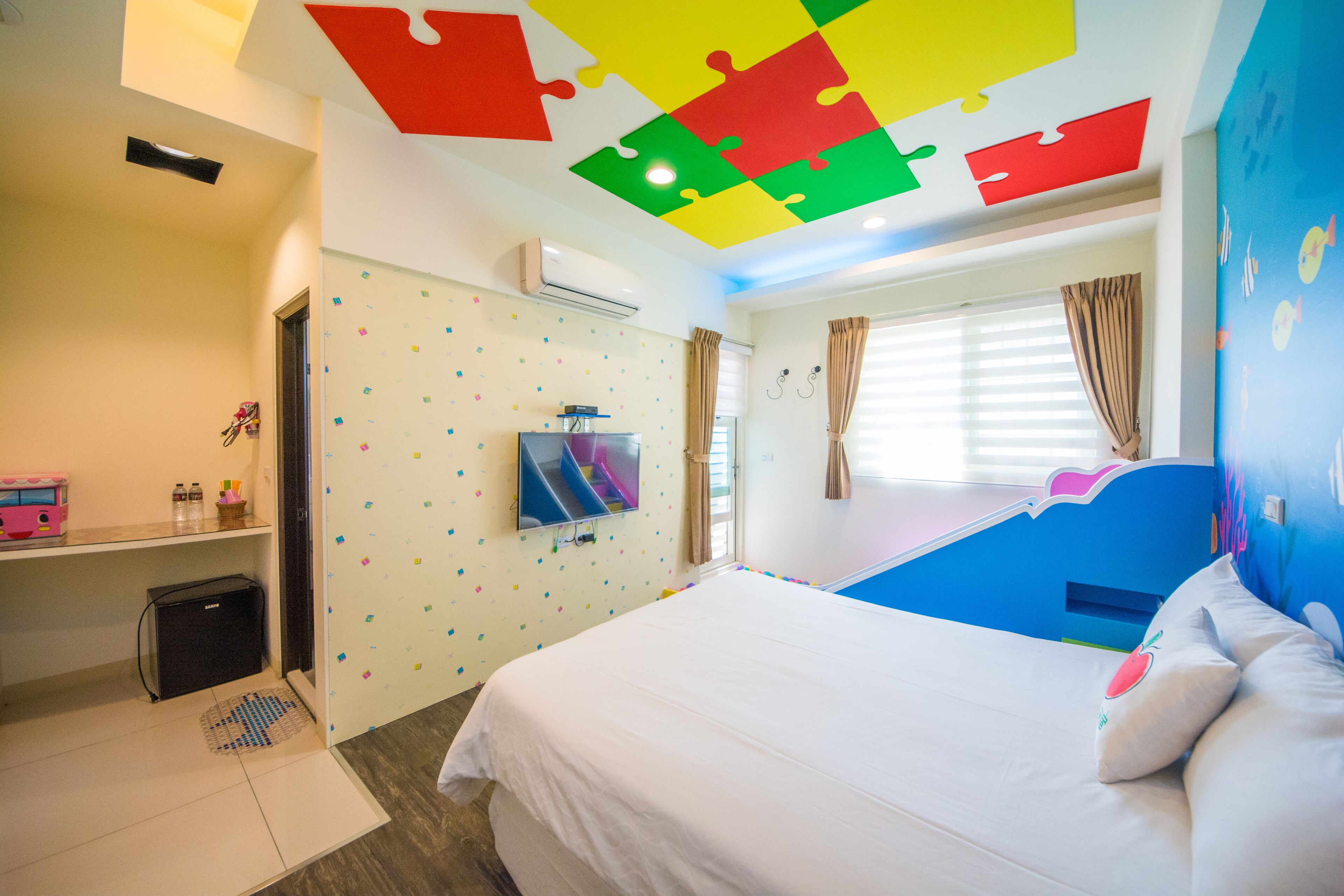 Habitación de hotel con cama, televisor, escritorio y ventana con cortinas.