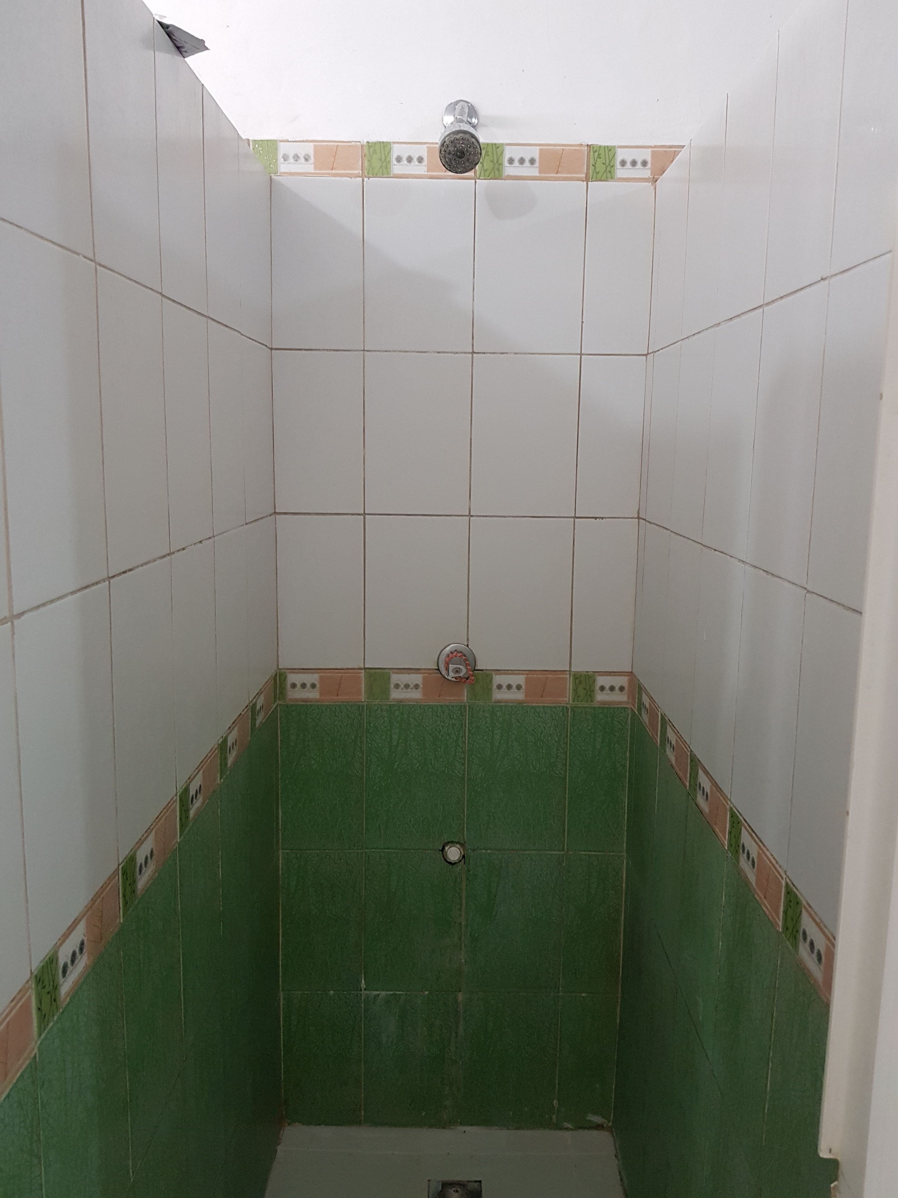 A small, tiled shower room with green and white tiles, a showerhead, and a drain.