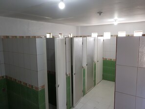 Fila de cabinas de baño blancas con paredes de azulejos verdes y suelos de baldosas blancas.