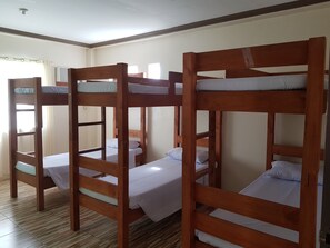 Una habitación con cuatro literas, cada una con colchón y almohada blancos, estructura de madera y una ventana con cortinas.