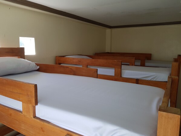 Un dormitorio con cuatro literas de madera, cada una con ropa de cama blanca.