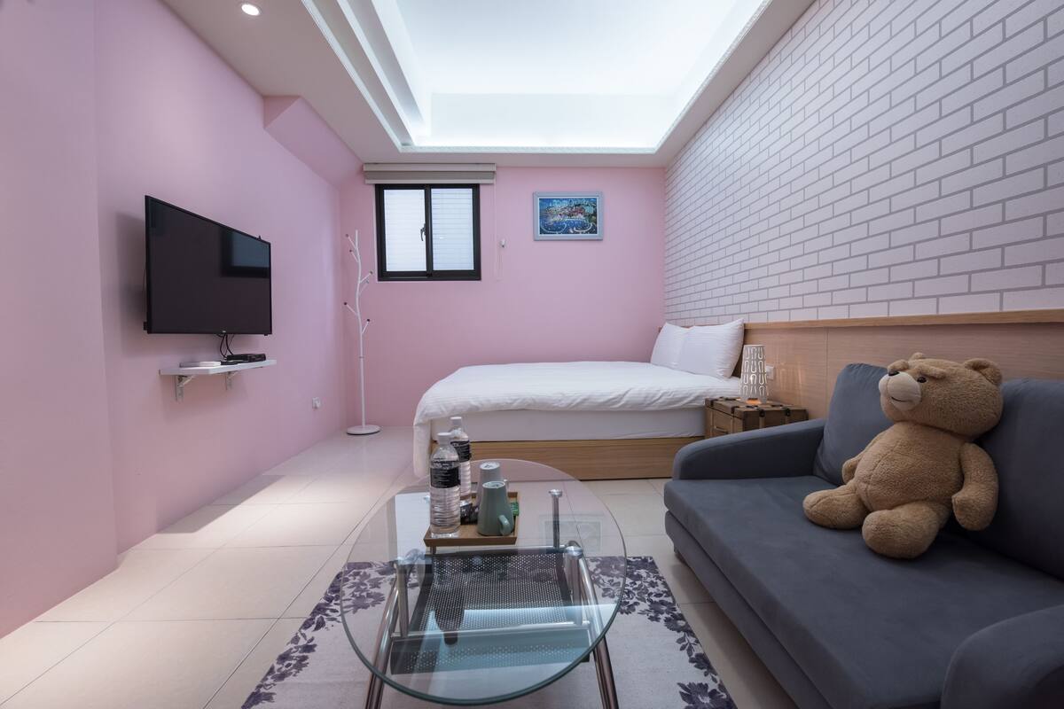 Un dormitorio moderno con tragaluz, una cama, un sofá, un televisor y un osito de peluche.