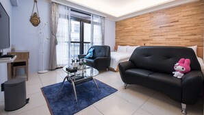 A modern living room with a black leather sofa, a glass coffee table, a blue rug, a wooden accent wall, and a large window with sheer curtains. - Cattleya B&B (Magong)