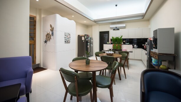 A modern dining area with round wooden tables and green chairs, a kitchen in the background, and a skylight above. - Cattleya B&B (Magong)