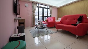 A pink-themed living room with a red sofa, a glass coffee table, a small round table, and a green ottoman. - Cattleya B&B (Magong)