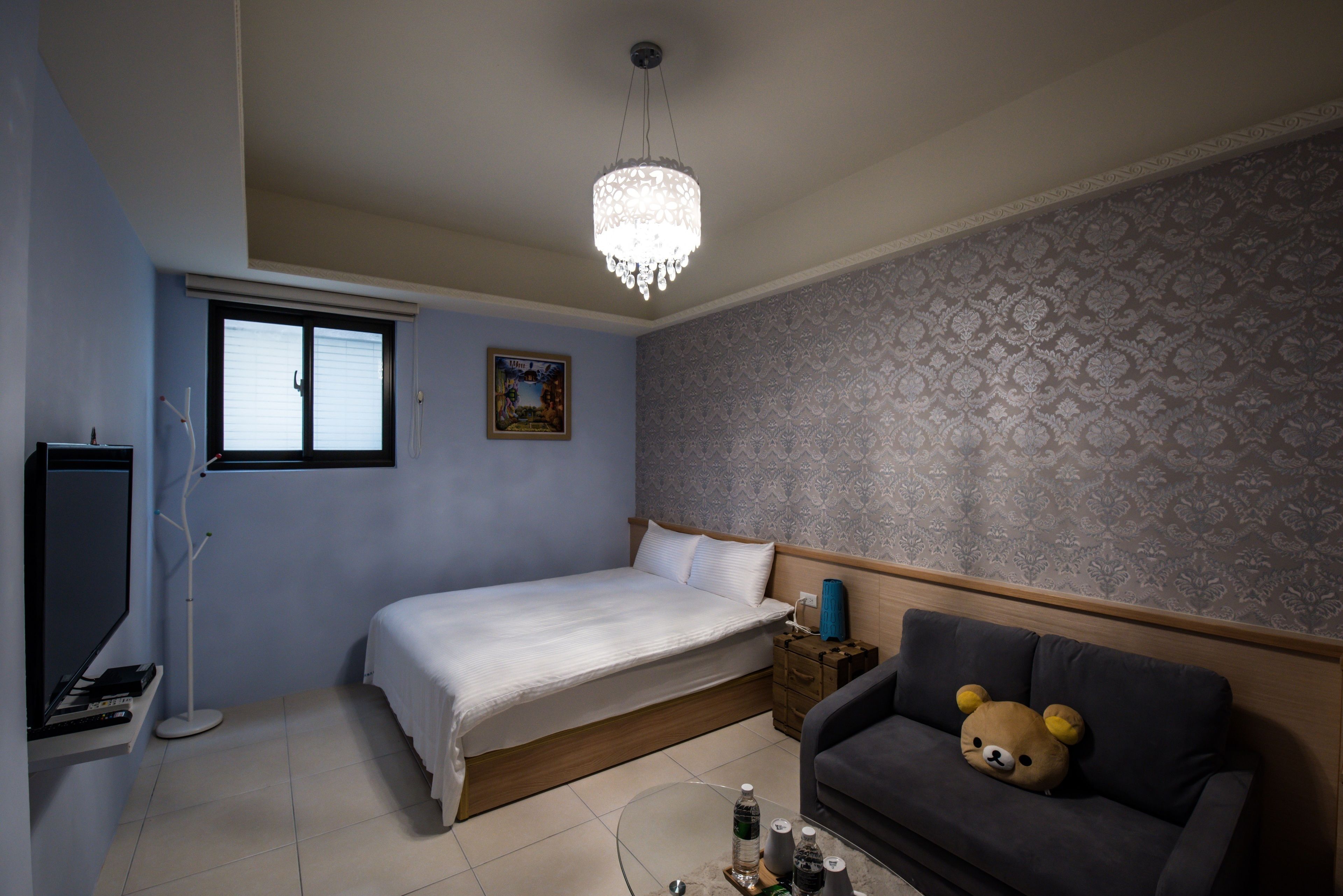 Une chambre à coucher avec un lit, un canapé, un lustre, une fenêtre et un mur orné d’un motif.