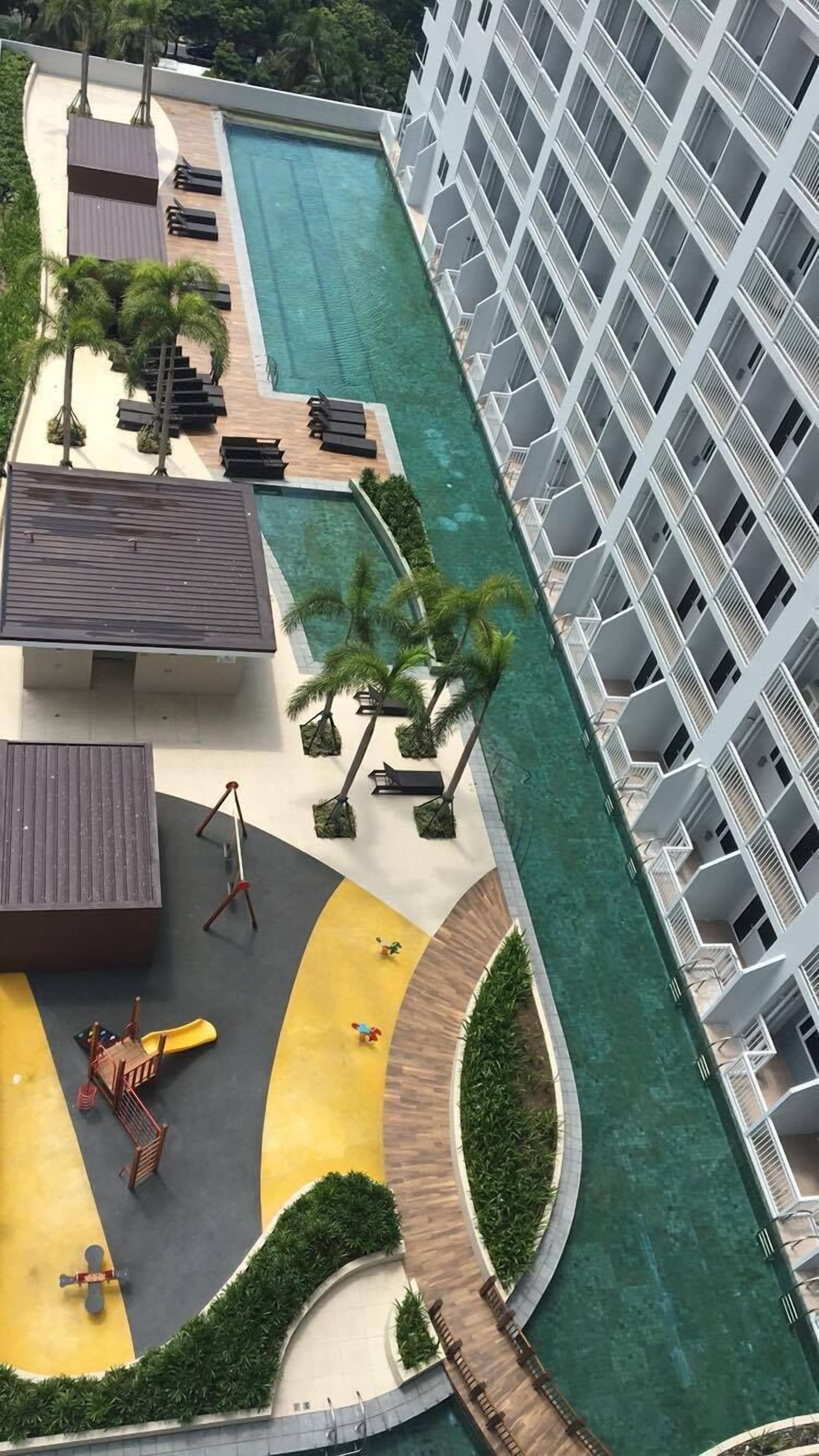 Un hôtel doté d’une piscine, de chaises longues, de palmiers et d’un espace de jeux pour enfants.